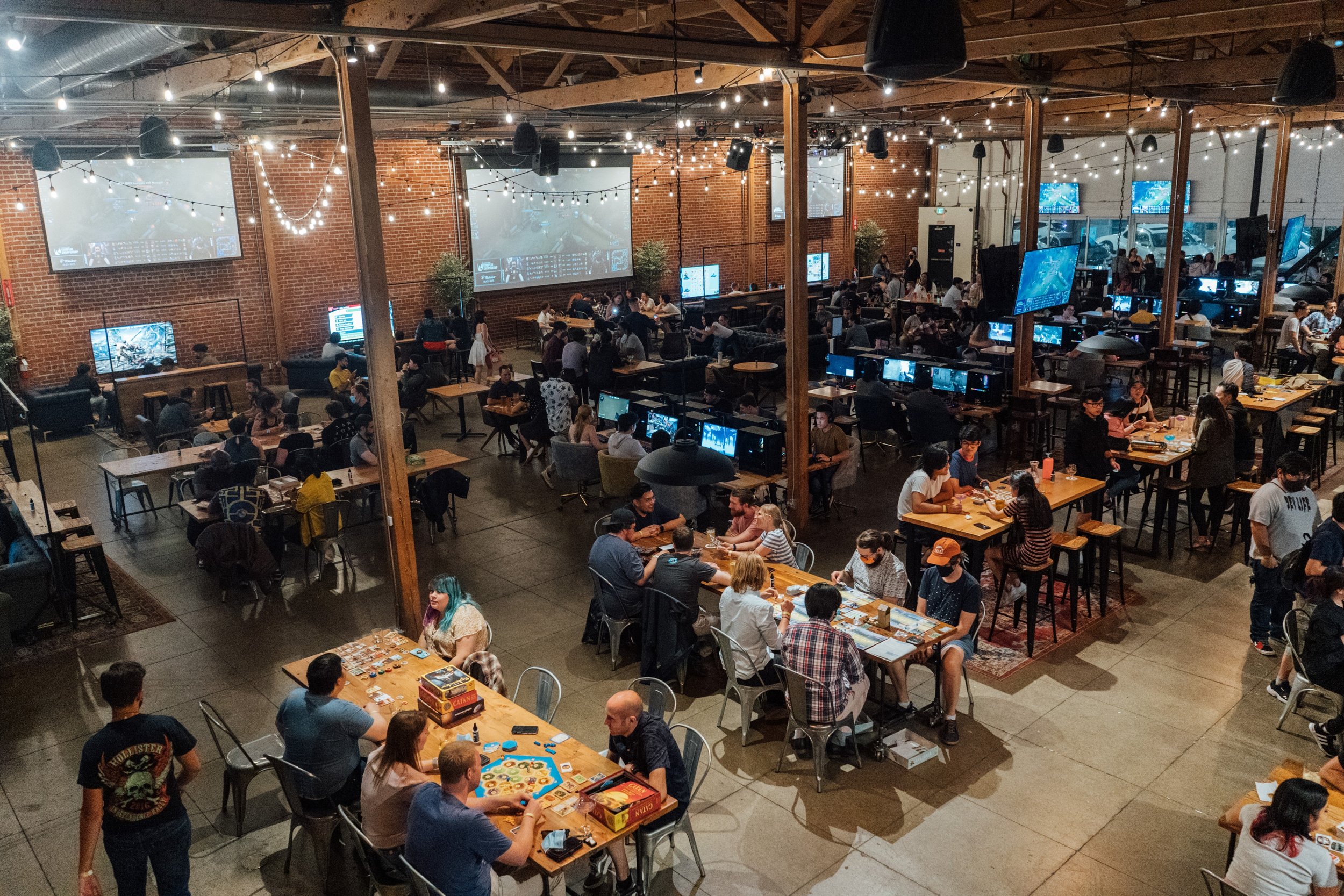 Guests gathering around game tables inside Guildhouse's brick-walled Great Hall